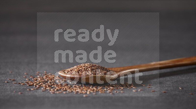 ملعقة خشبية كبيرة ممتلئة بحبوب بذر الكتان وبعض البذور متناثرة علي خلفية سوداء