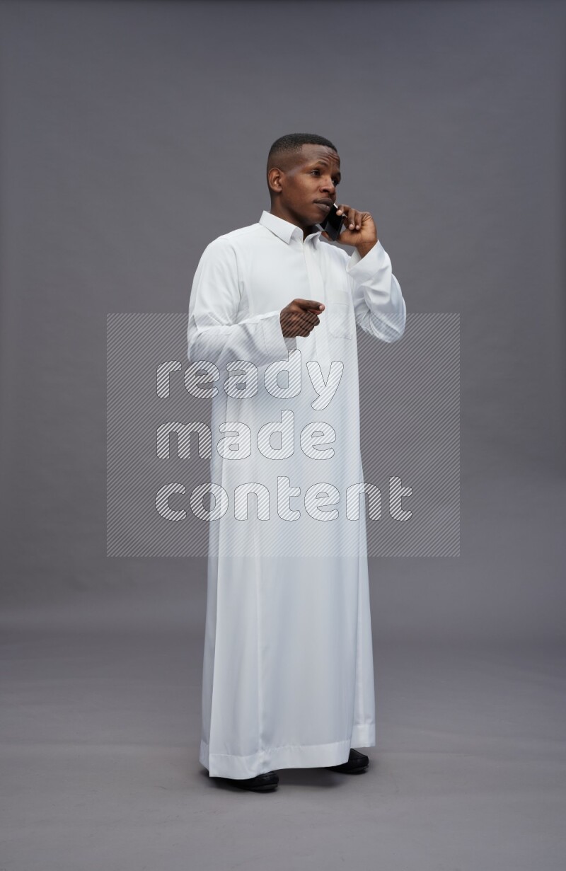 Saudi man wearing thob standing talking on phone on gray background