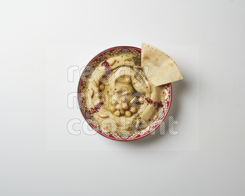 Hummus in a red plate with patterns garnished with zaatar & sumak on a white background