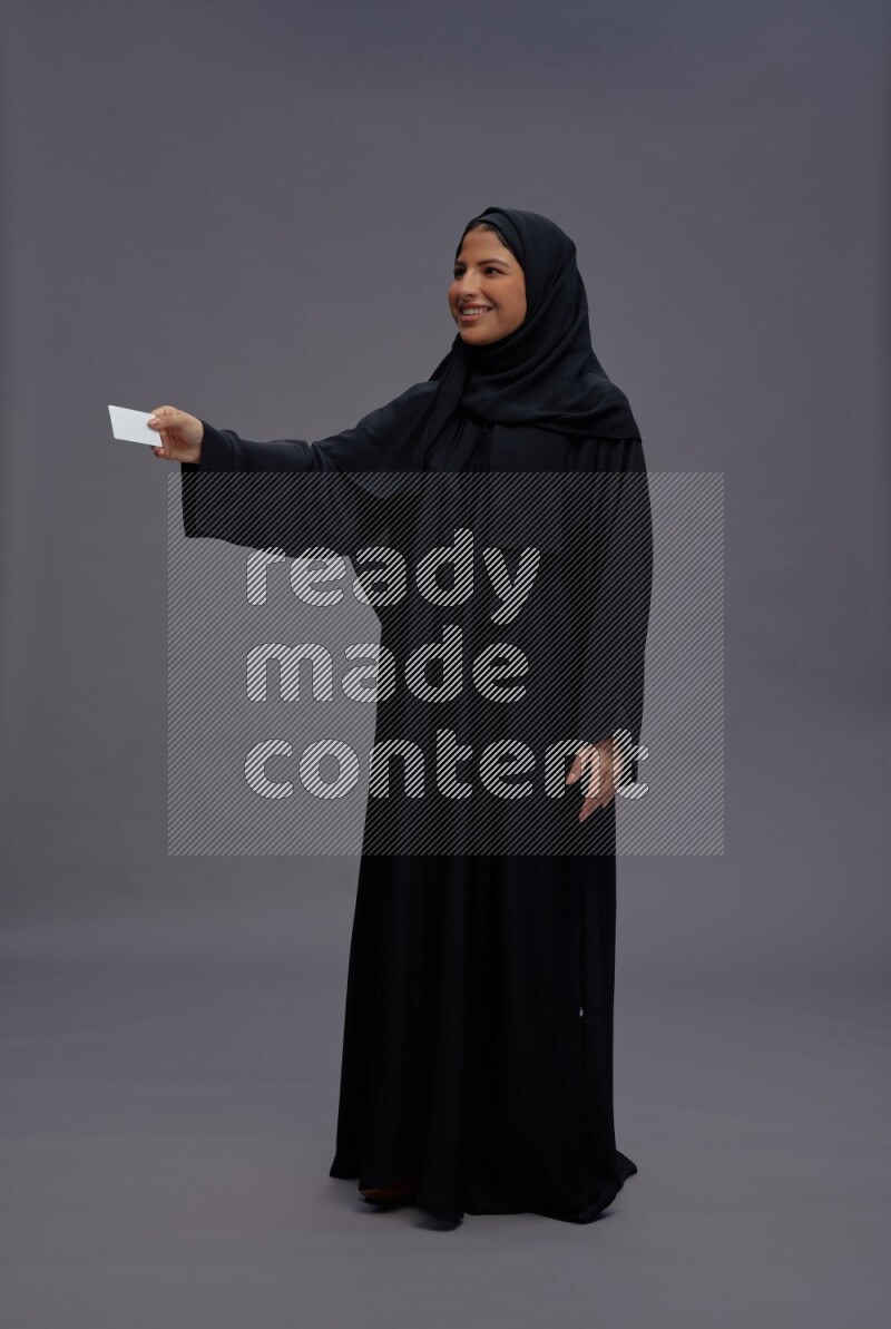 Saudi woman wearing Abaya standing holding ATM card on gray background
