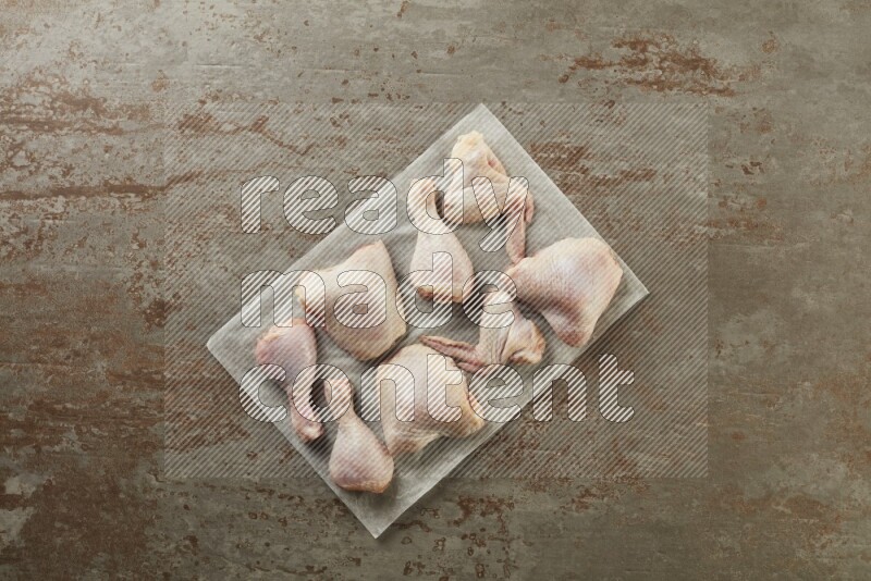 Mixed fresh chicken pieces on a parchment paper direct on a textured rustic background