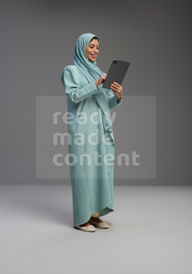 Saudi Woman wearing Abaya standing working on tablet on Gray background