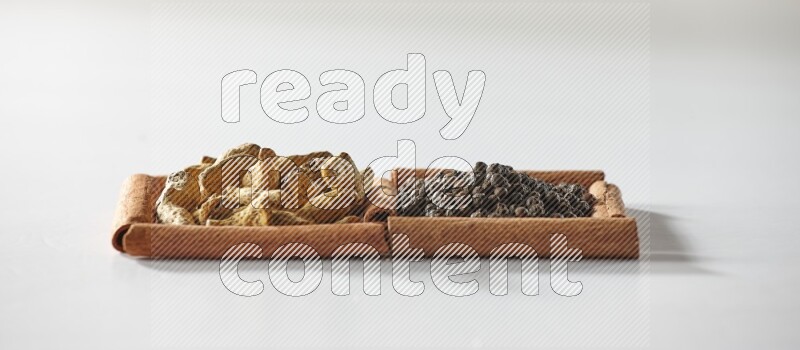 2 squares of cinnamon sticks full of black peppers and turmeric fingers on white flooring