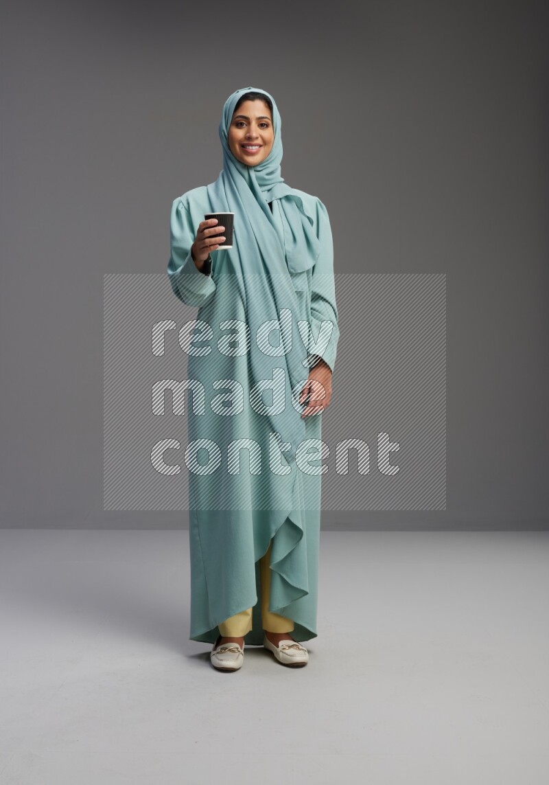 Saudi Woman wearing Abaya standing  holding paper cup on Gray background