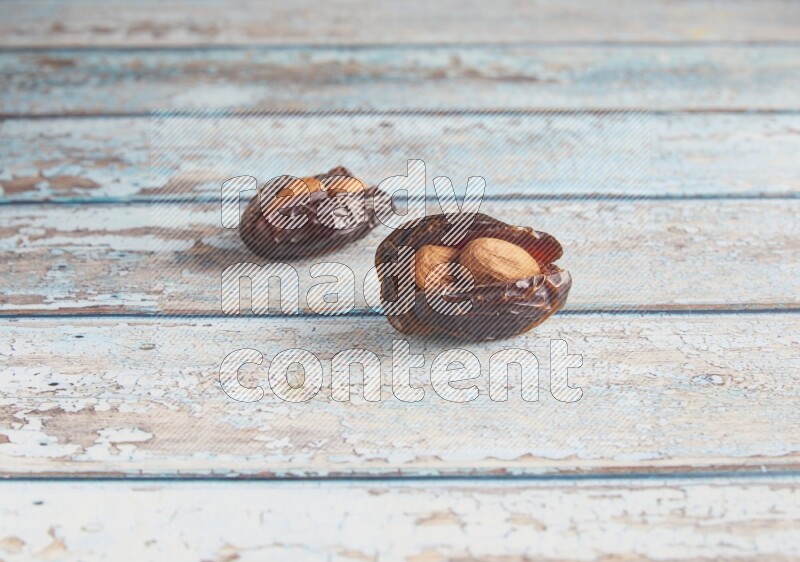 two almond stuffed madjoul dates on a light blue wooden background