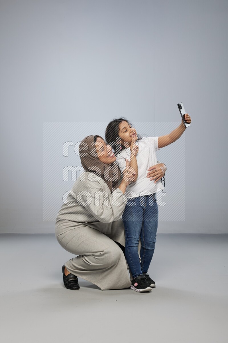 A girl standing taking selfie with her mother on gray background