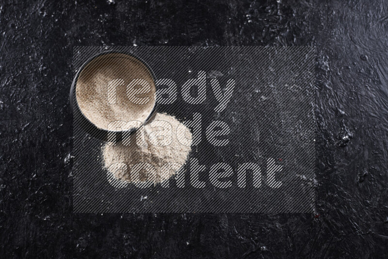 A black pottery bowl full of onion powder with fallen powder from it on black background