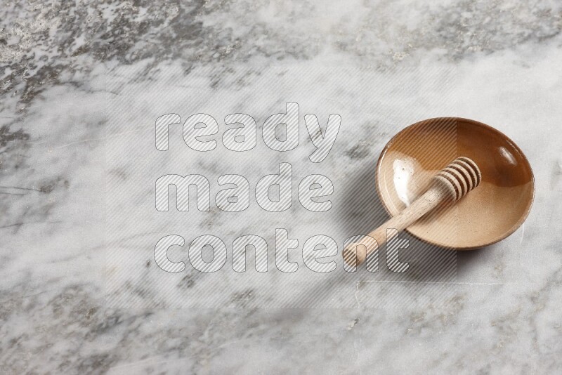 Multicolored pottery plate with wooden honey dipper in it on grey marble background
