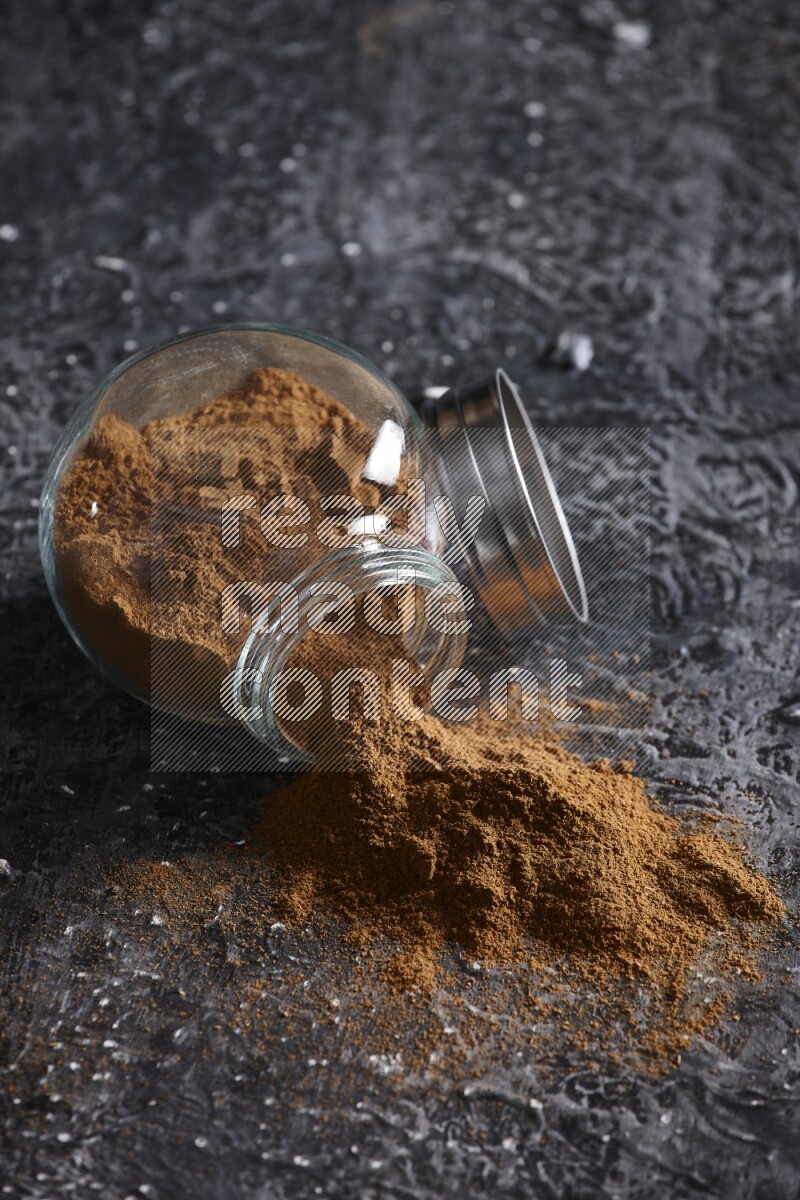 Flipped herbal glass jar full of cinnamon powder on textured black background
