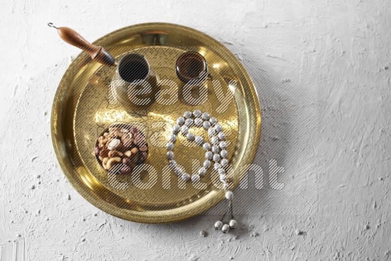 Nuts in a metal bowl with coffee and prayer beads on a tray in a light setup
