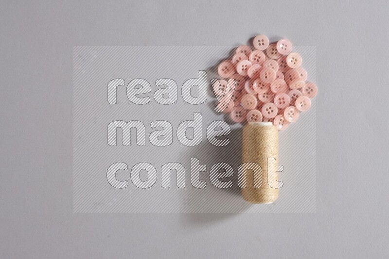 بكرة خيط خياطة بيج مع مجموعة صغيرة من الأزرار على خلفية رمادية