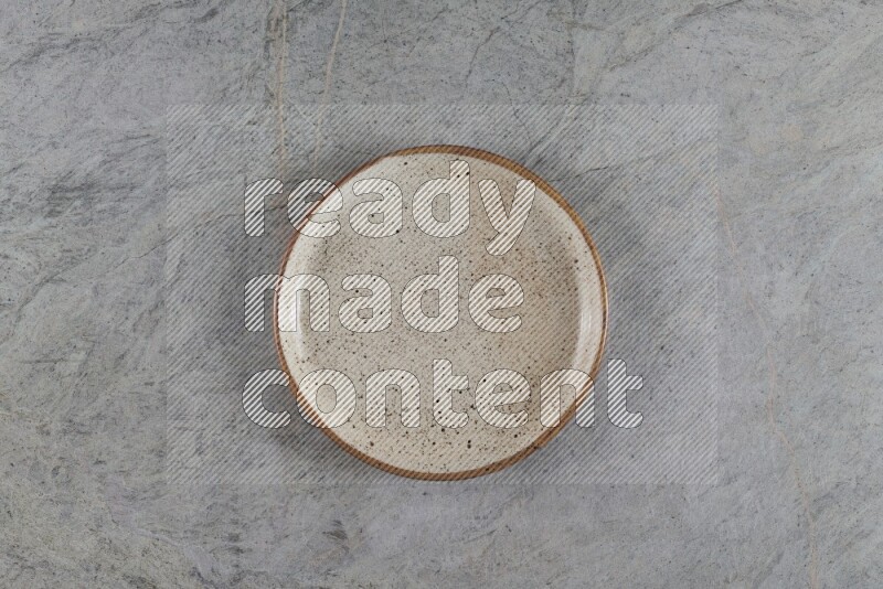 A circular beige pottery plate on grey marble background