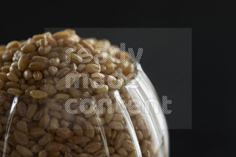 Hulled wheat in a glass jar on black background
