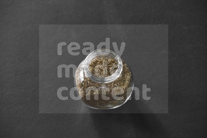 A glass spice jar full of cumin on black flooring