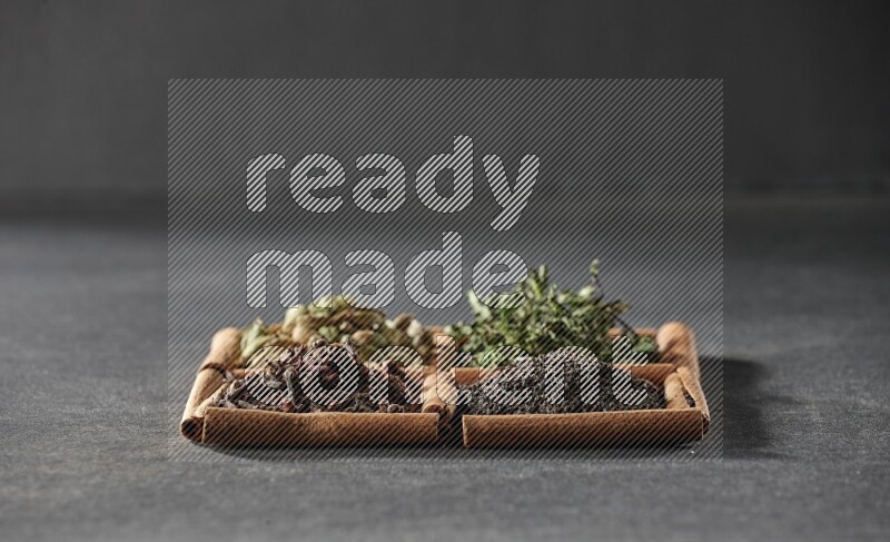 4 squares of cinnamon sticks full of black tea, cloves, dried mint leaves and cardamom on black flooring