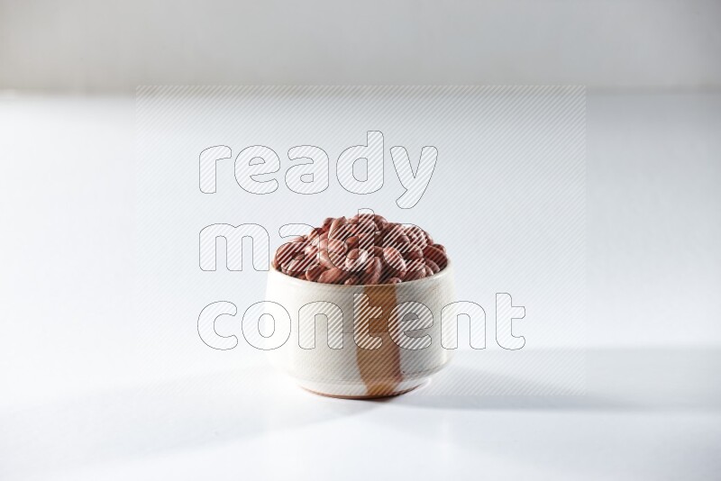 A beige ceramic bowl full of red skin peanuts on a white background in different angles