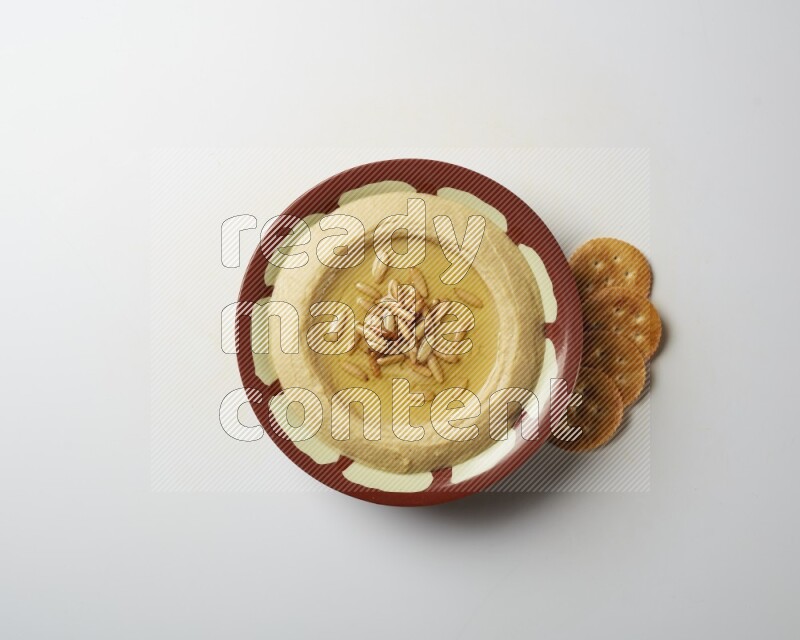 Hummus in a traditional plate garnished with pine nuts on a white background