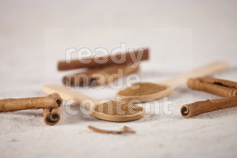 Two wooden spoons full of cinnamon powder with cinnamon sticks on white background