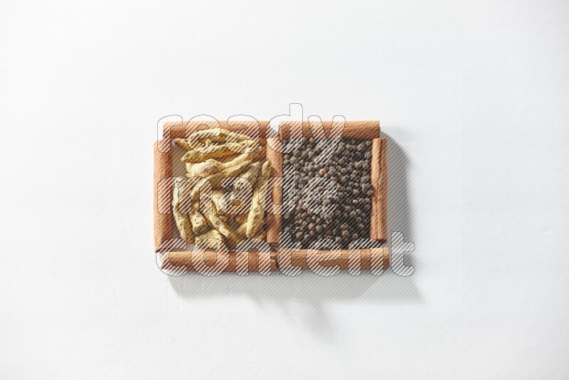 مربعان من أعواد القرفة ممتلئان بحبوب الفلفل الأسود وأصابع الكركم علي خلفية بيضاء