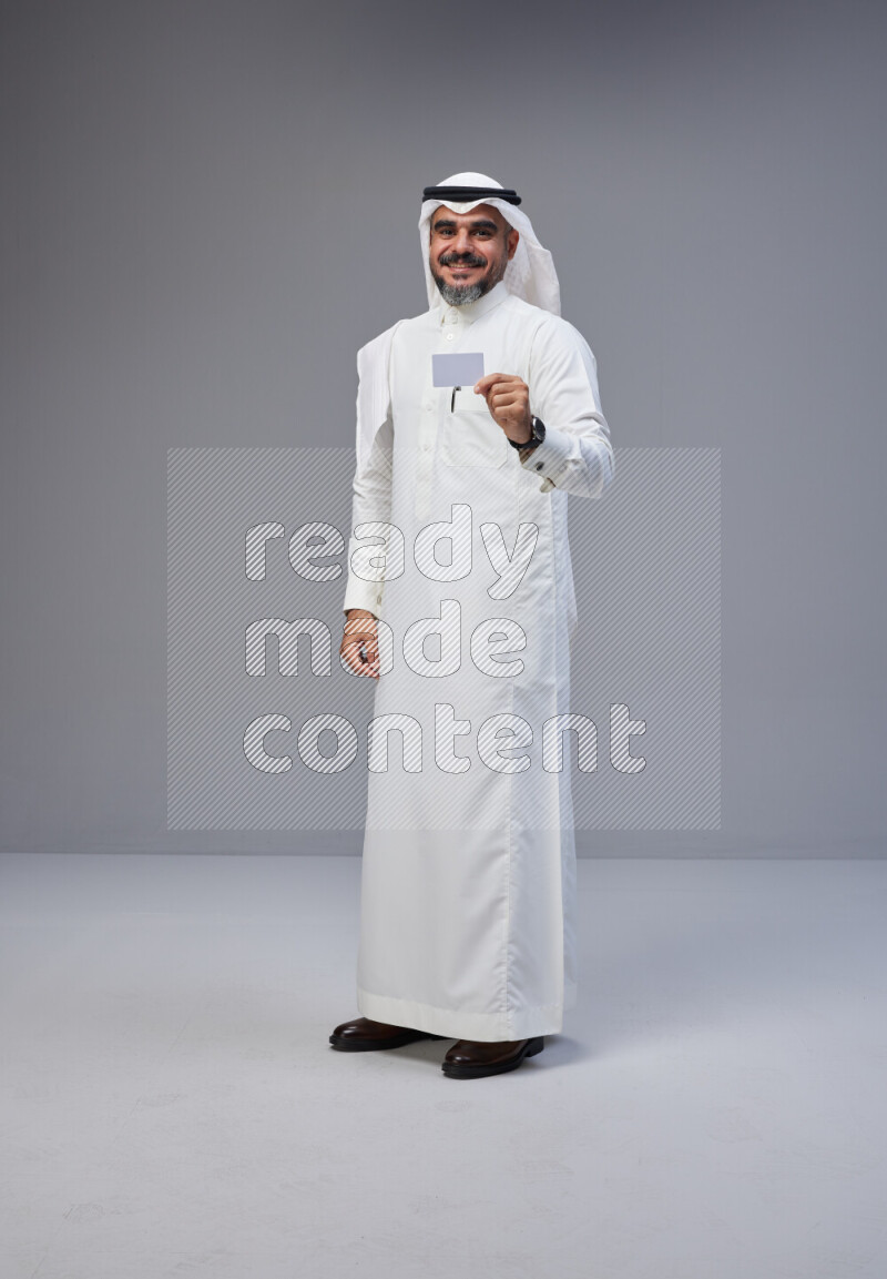 Saudi man Wearing Thob and white Shomag standing holding ATM card on Gray background