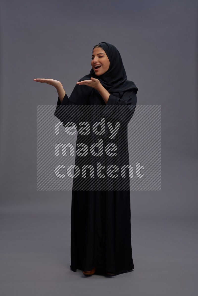 Saudi woman wearing Abaya standing interacting with the camera on gray background