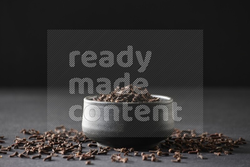 وعاء فخاري أسود ممتلئ بحبوب القرنفل علي خلفية سوداء