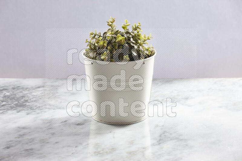 Green artificial plant in white pot on light grey marble background