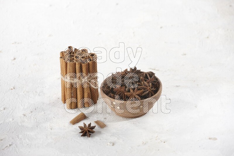 A stacked and bounded cinnamon sticks and a wooden bowl full of star anise on a white background