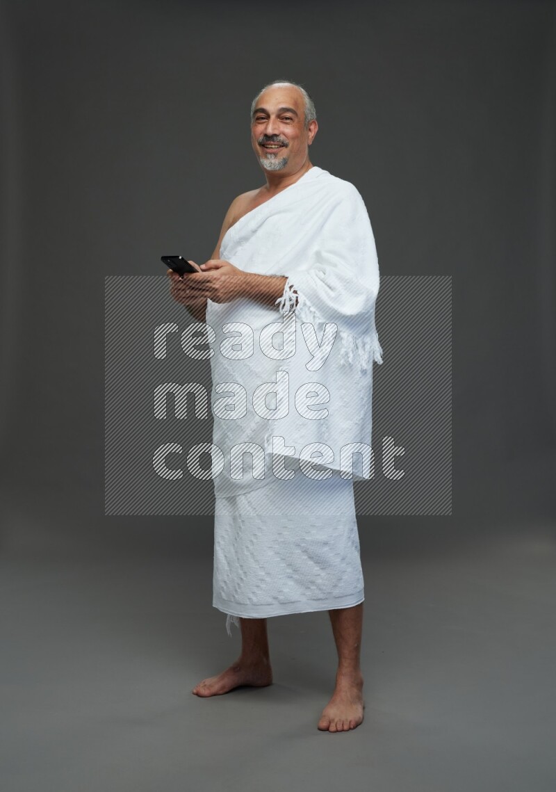 A man wearing Ehram Standing texting on phone on gray background