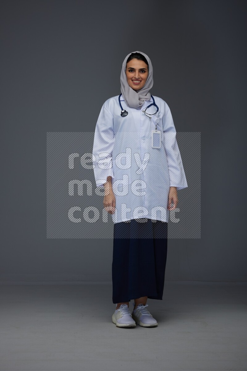 A female doctor wearing a light gray head scarf standing on grey background.