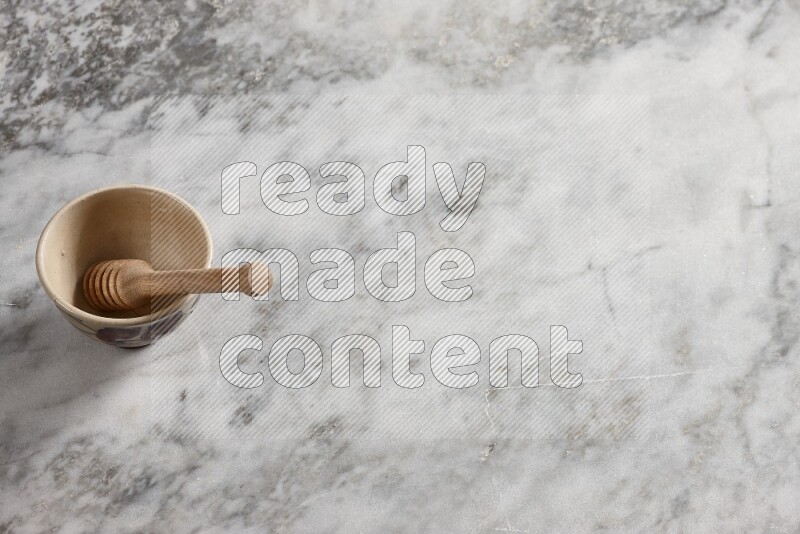 Decorative pottery bowl with wooden honey dipper in it on grey marble background