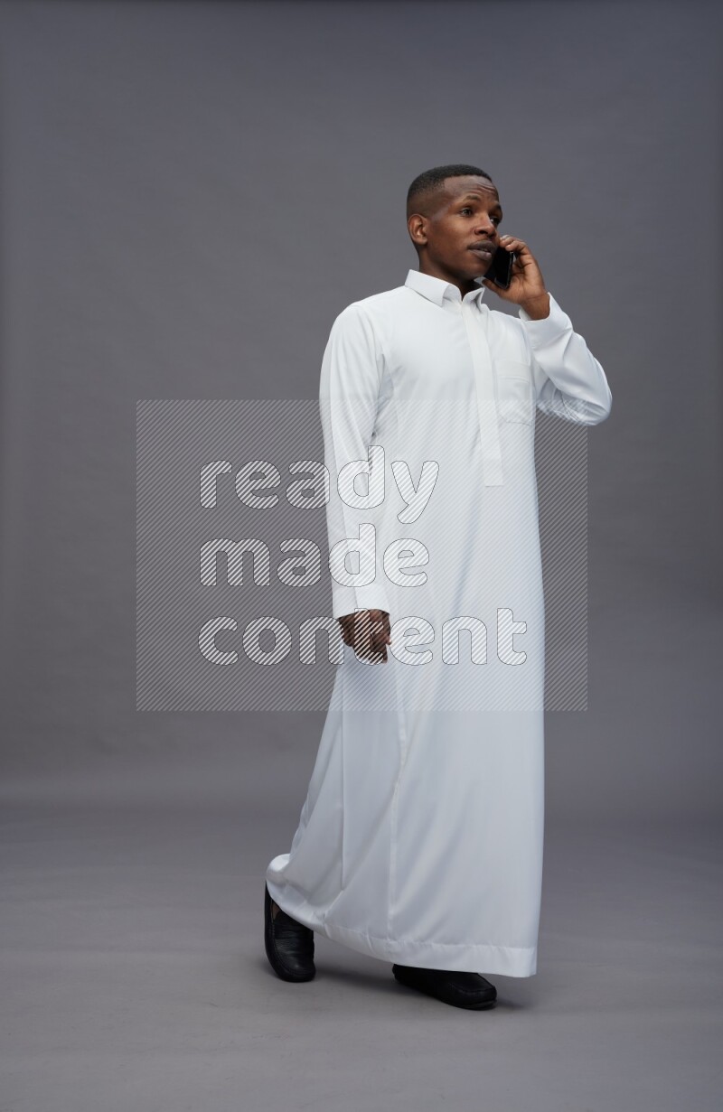 Saudi man wearing thob standing talking on phone on gray background