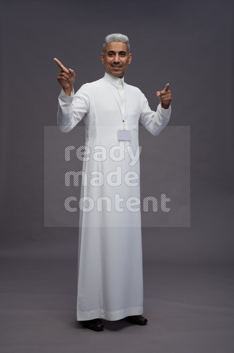 Saudi man wearing thob with neck strap employee badge standing interacting with the camera on gray background