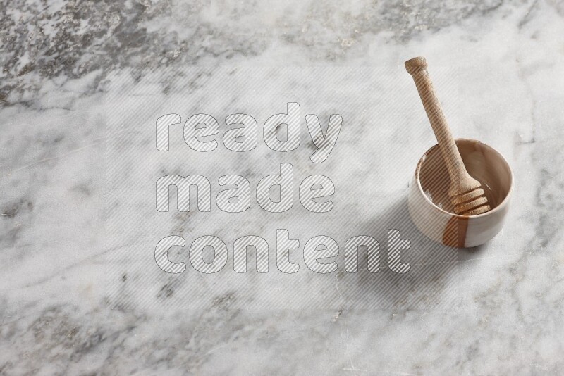 Beige pottery bowl with wooden honey dipper in it on grey marble background