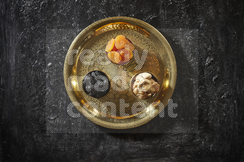 Dried fruits in metal bowls on a tray in a dark setup