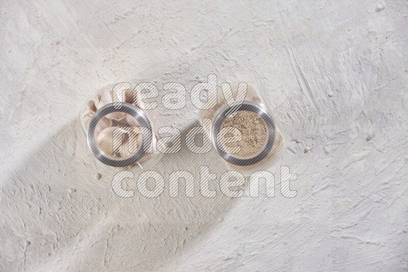 وعاءان زجاجيان احدهما ممتلئ ببودرة الثوم والأخر ممتلئ بفصوص الثوم علي خلفية بيضاء