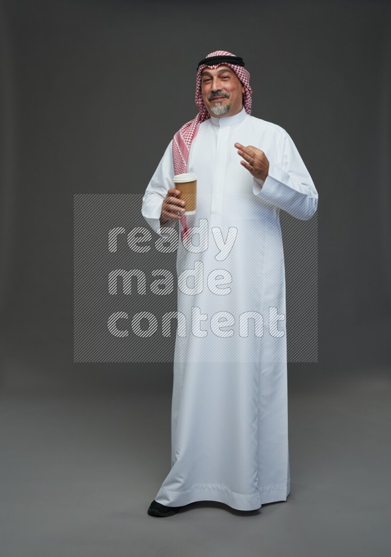 Saudi man with shomag Standing holding paper cup on gray background