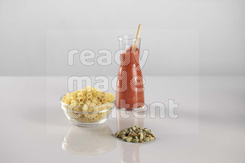 Raw pasta with tomatoe pasta with different ingredients such as cherry tomatoes, basil, garlic, bay laurel, cardamom, white pepper, black pepper, red chilis and wheat stalks on light grey background