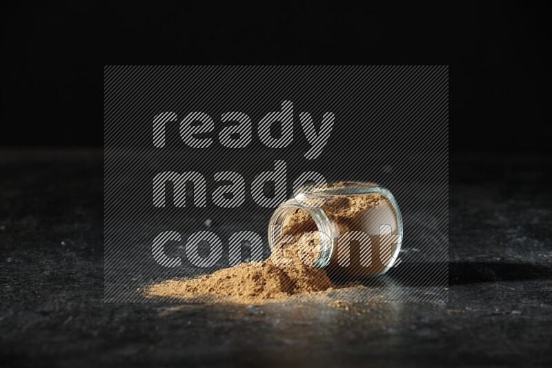 وعاء زجاجي للتوابل مقلوب ممتلئ ببودرة بهار الفلفل الحلو والبودرة تناثرت منه على خلفية سوداء