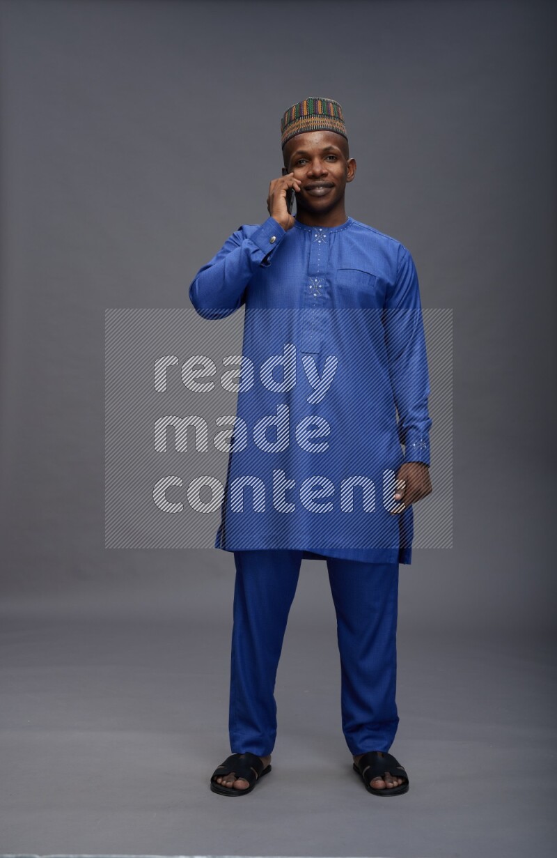 Man wearing Nigerian outfit standing talking on phone on gray background