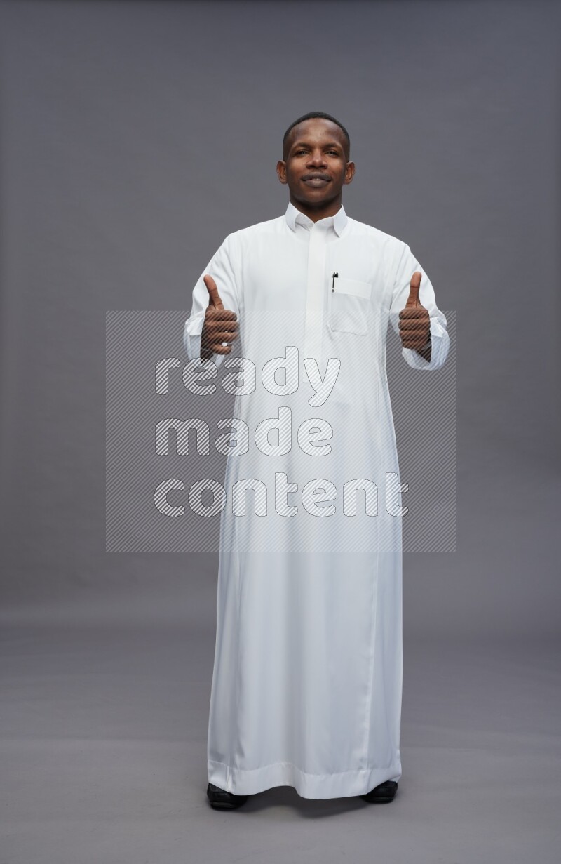 Saudi man wearing thob standing interacting with the camera on gray background