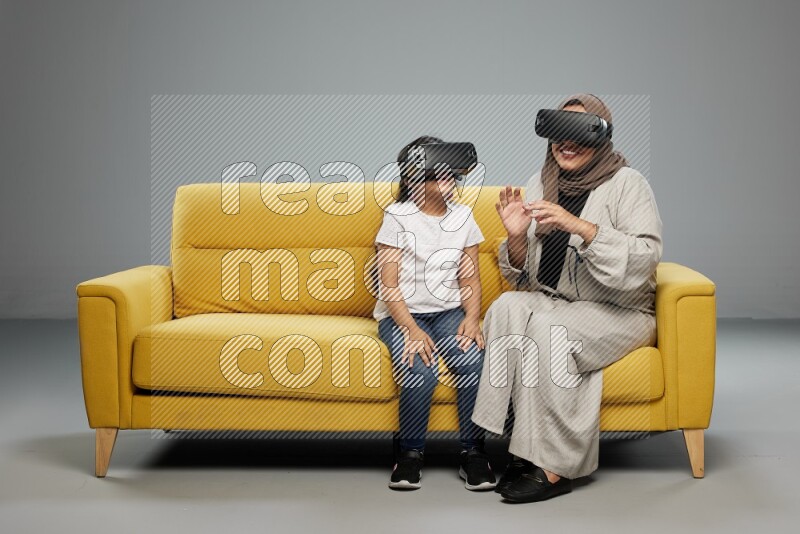 A girl and her mother sitting playing with VR on gray background