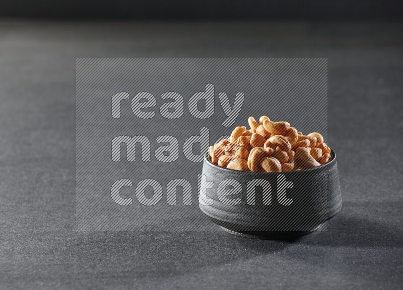 A black pottery bowl full of cashews on a black background in different angles