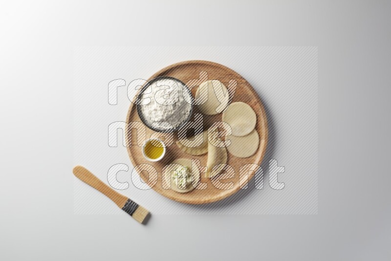 two closed sambosas and one open sambosa filled with cheese while flour, and oil with oil brush aside in a wooden dish on a white background