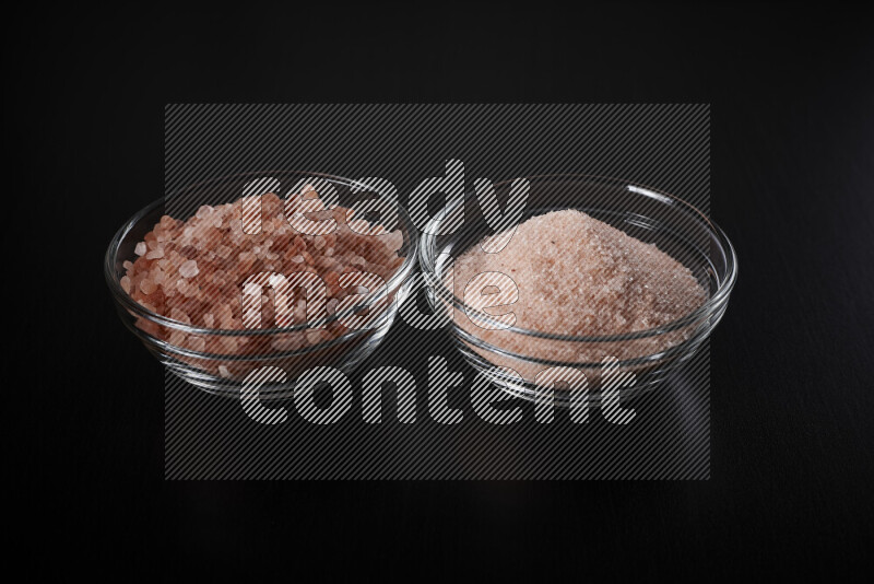2 glass bowls one is filled with fine himalayan salt and the other with coarse himalayan salt on black background