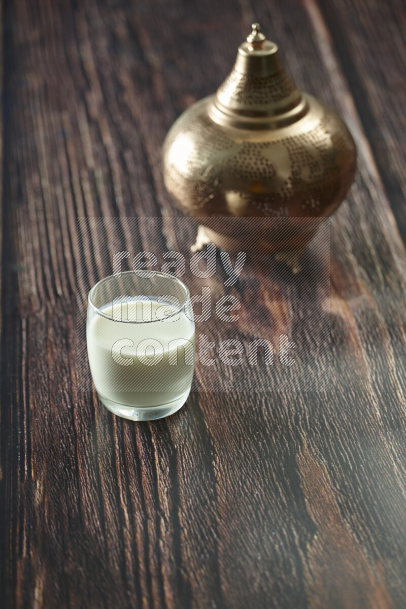 A golden lantern with different drinks, dates, nuts, prayer beads and quran on brown wooden background