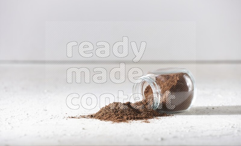 A flipped glass spice jar full of cloves powder and powder came out of it on textured white flooring