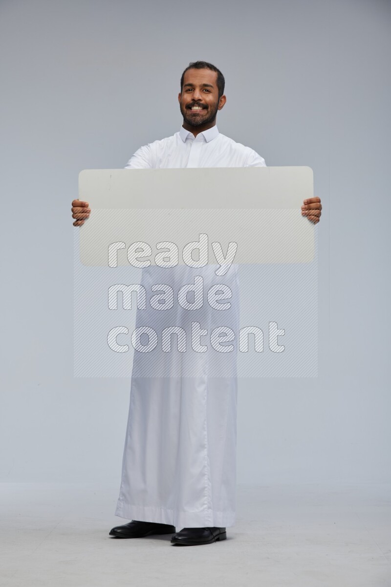 Saudi man wearing Thob standing holding board on Gray background