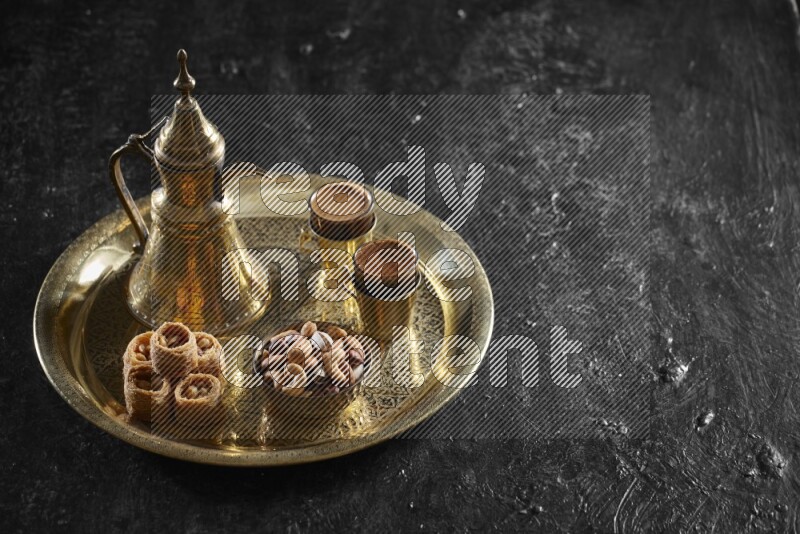 Oriental sweets with nuts and a drink on a metal tray in a dark setup