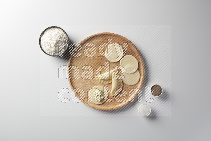 two closed sambosas and one open sambosa filled with cheese while flour, salt, and black pepper aside in a wooden dish on a white background